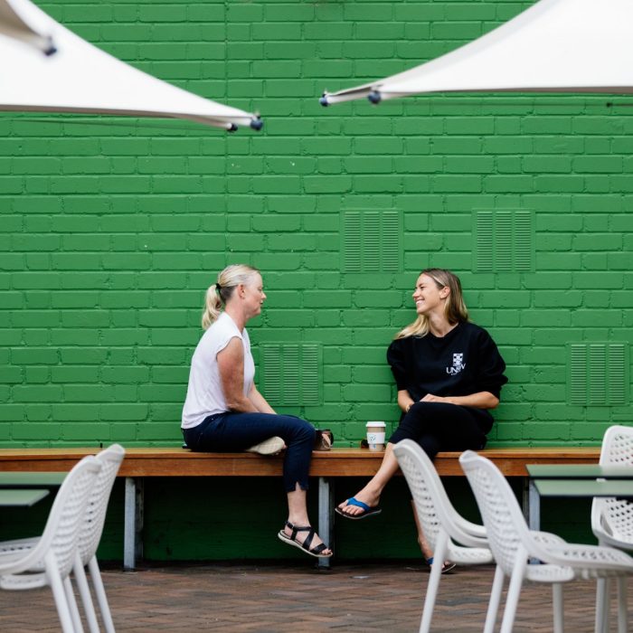 Two women in conversation Two women sit on a bench seat at an outdoor cafe, having a conversation