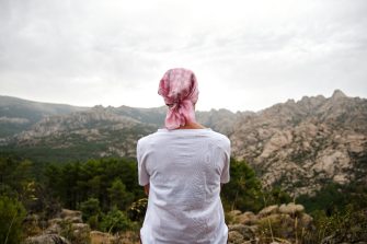 1448305574 Woman with cancer sitting in a natural space. She wears a pink scarf on her head