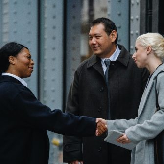 Two women shaking hands standing next to a man