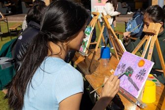 Students painting canvasses on easels in an outdoor setting. 