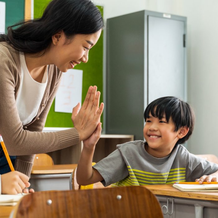 Young Asian teacher giving boy high five in school, success, achievement, happiness. Asia school boy with young woman in class.