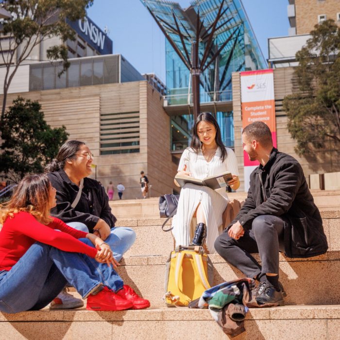 A group of four students sitting on steps of the university walkway