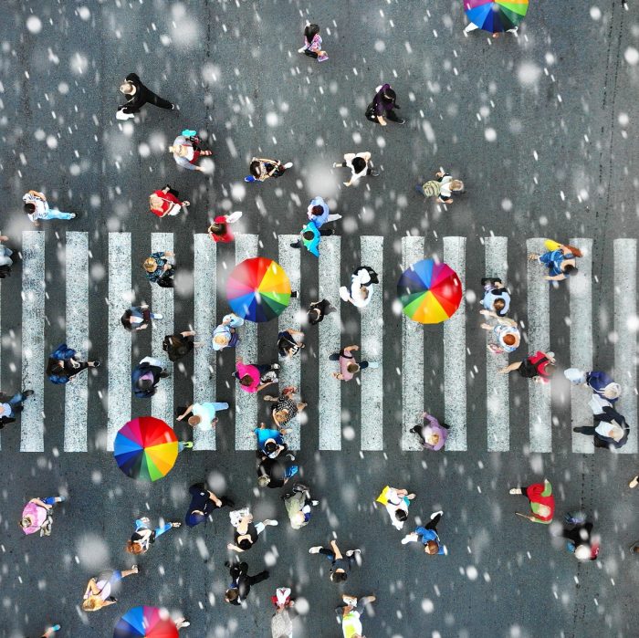 Aerial. People crowd on a pedestrian crossing crosswalk when it's rain. View above.