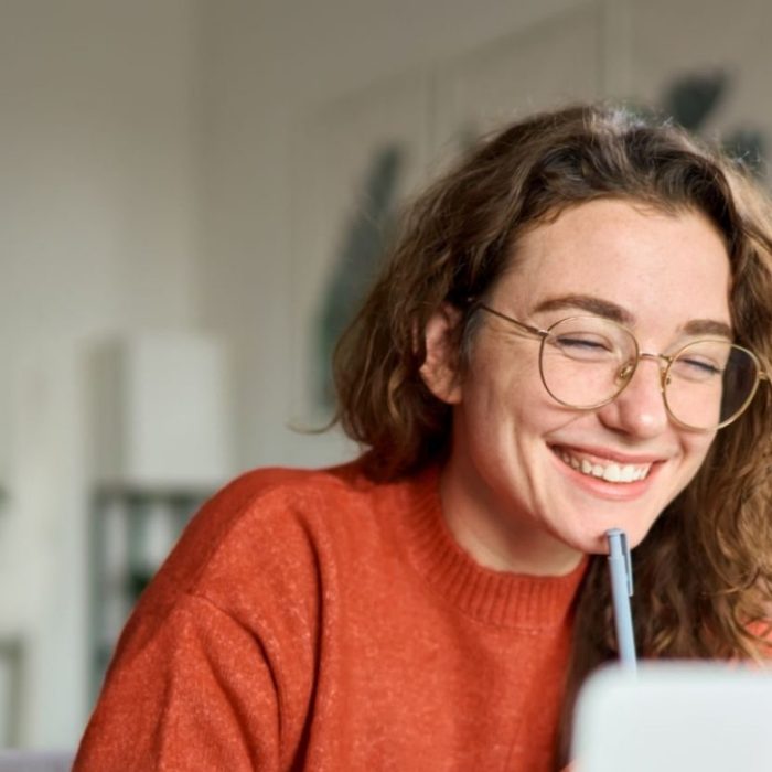 Happy young woman using laptop sitting at desk writing notes while watching webinar, studying online, looking at pc screen learning web classes or having virtual call meeting remote working from home.