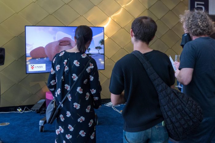 Guests and team members mingling around visual presentation and socialising in foyer of John Clancy Auditorium UNSW Sydney 