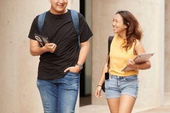 2 students walking with laptops and backpacks