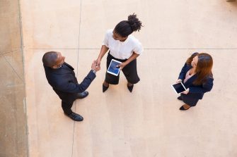 3 business people with iPads talking and shaking hands dressed in business attire