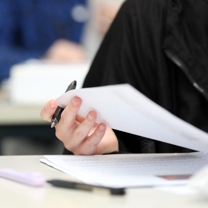 A close up isolated students hand holding a pen checking their answers during class, exam or lesson time at school. Bright colors and second student blurred in the background