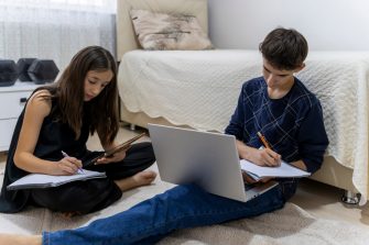 One man, young boy is tired of doing homework, sitting at the table, using laptop.