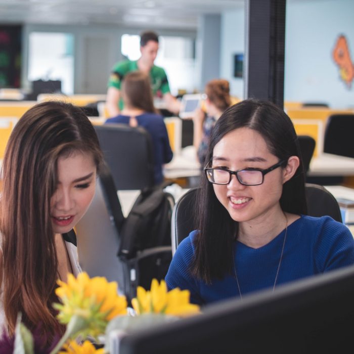 Two women smiling in front of a computer monitor