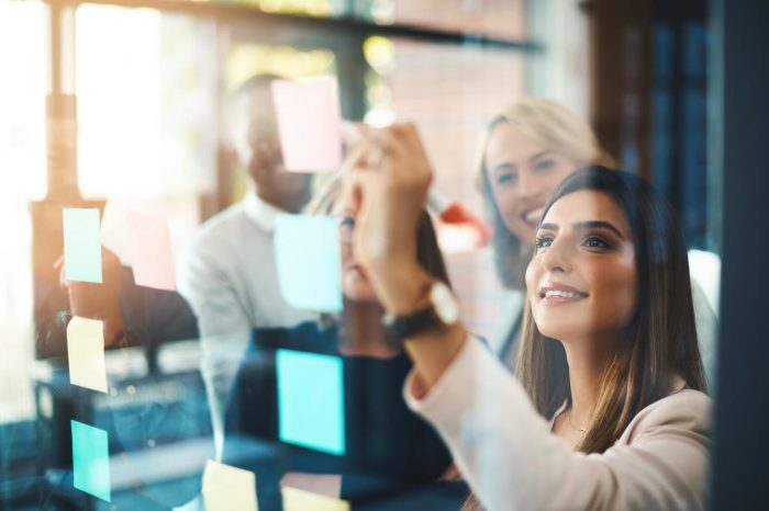 Shot of a group of businesspeople arranging sticky notes on a glass wall in a modern office