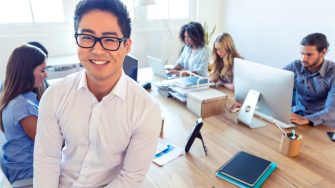 Young Asian business manager standing in front of his team in an office setting.