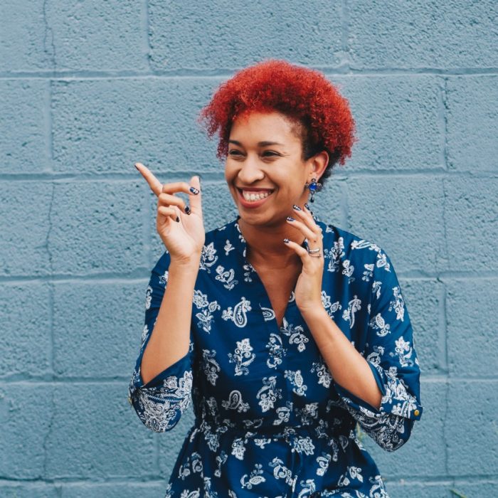 Woman with red hair smiling and pointing in front of a blue wall