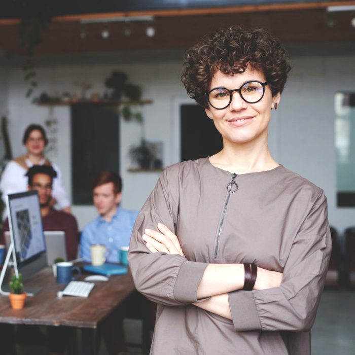 Photo of woman wearing eyeglasses with co-workers in the background