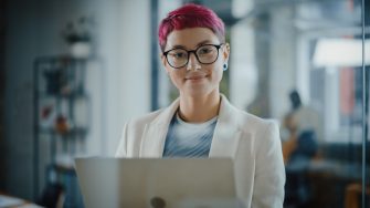 Modern office specialist with short pink hair standing holding laptop - stock photo