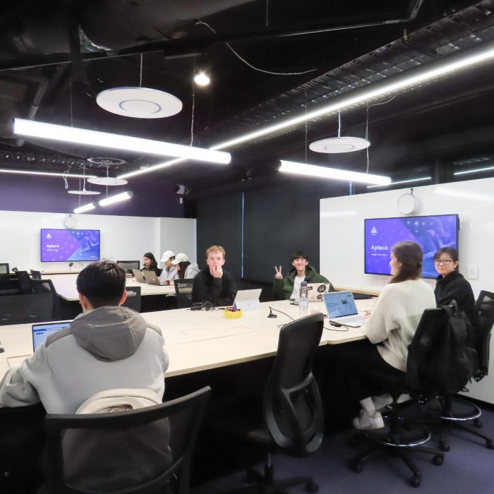 Students sitting on a desk with a large monitor