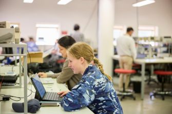 Student in military uniform studying on a laptop in a classroom