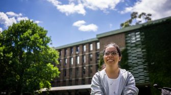 A student smiling while sitting on the grass on Library Lawn on Kensington Campus