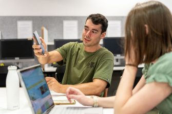 Students using their phones and laptops while sitting around a table