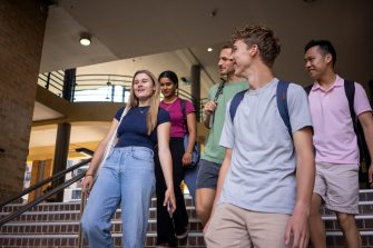 A group of students chatting while walking down a staircase in front of the Quad Food Court