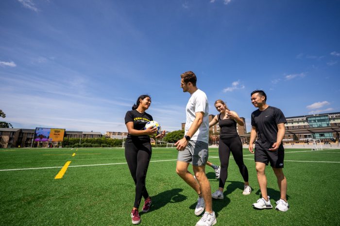 A group of students talking while walking on The Village Green's all-weather field