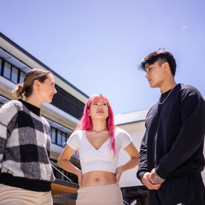 Three students standing and chatting on Paddington Campus against a backdrop of buildings and a bright blue sky