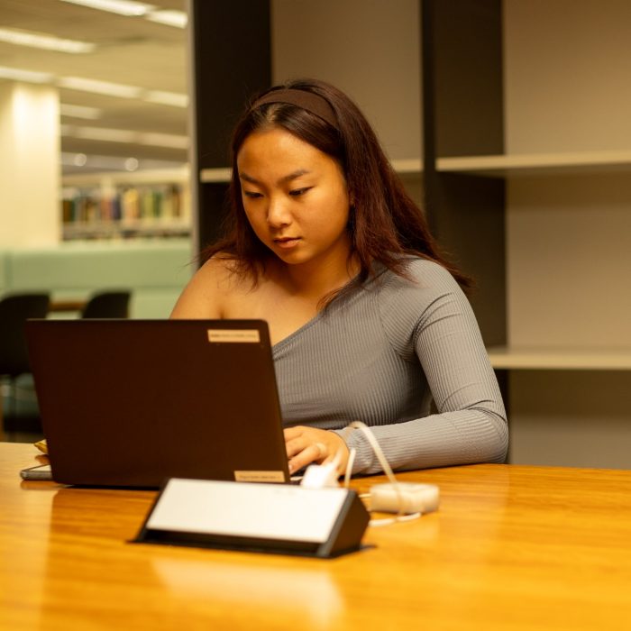 Students using their laptops at a shared desk in the library