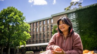 A student smiling while sitting on the grass on Library Lawn on Kensington Campus