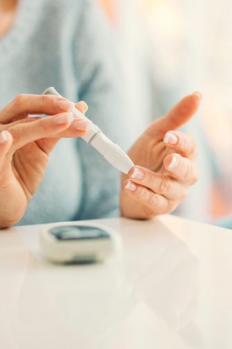 Woman with diabetes doing blood sugar test at home in a living room. 