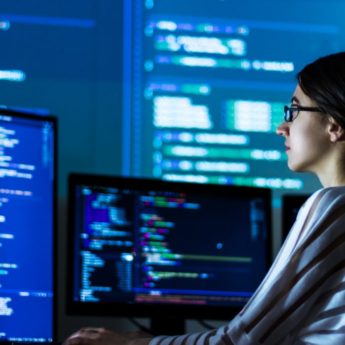 Software developer freelancer woman female in glasses work with program code C++ Java Javascript on wide displays at night Develops new web desktop mobile application or framework Projector background