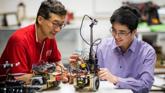 A UNSW academic helping a student at a work station with electrical components for a robotic vehicle