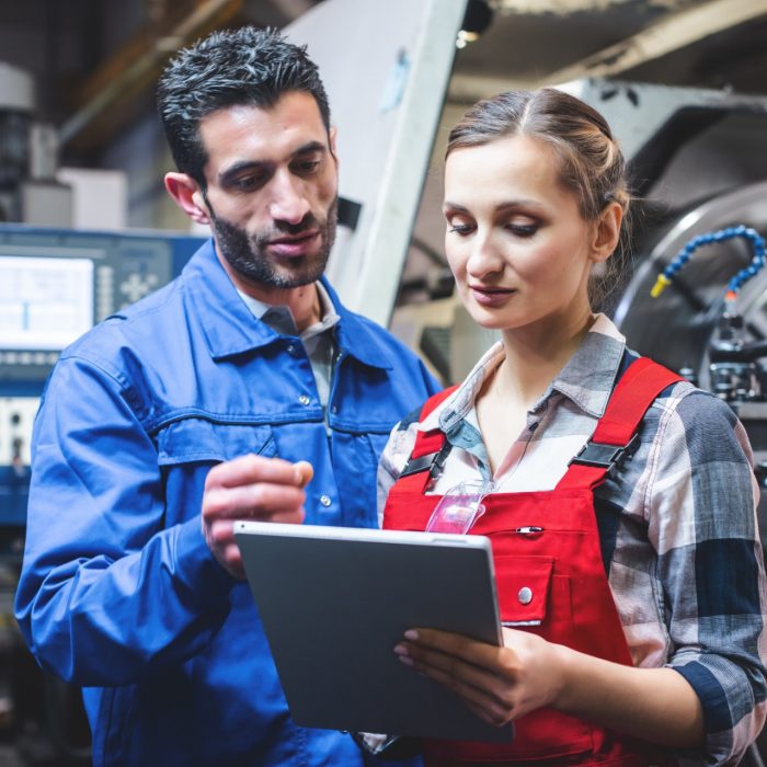 Woman and man manufacturing worker in discussion writing on tablet computer