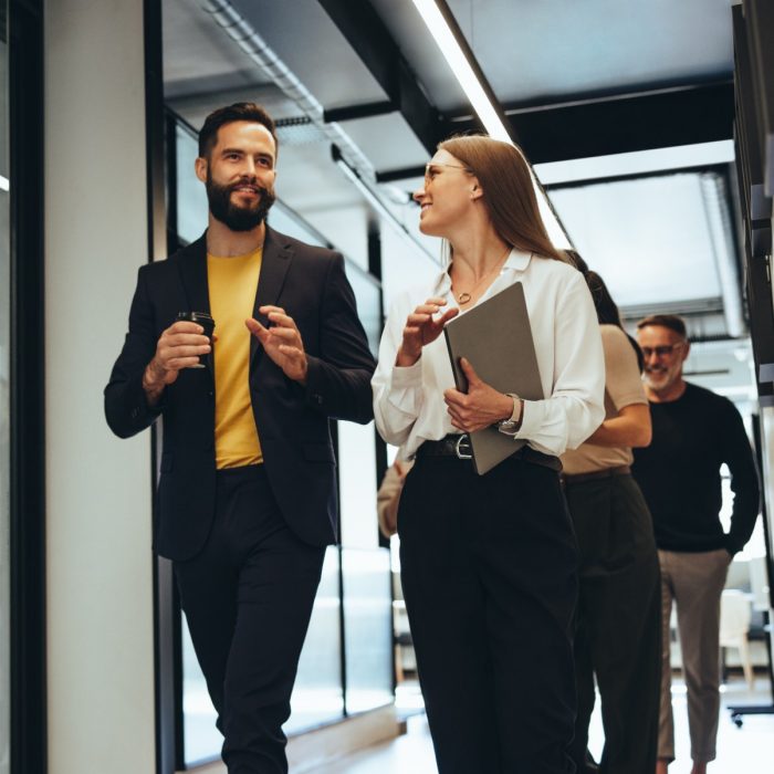 Young professionals having a discussion in a modern office. Two happy young businesspeople smiling while walking together in a hallway. Cheerful colleagues collaborating on a new project.