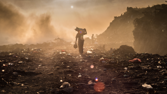 Plastic waste picker carrying rubbish at landfill site.