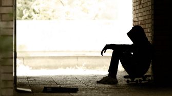 Silhouette of  Lonely Teenager Sitting in the Dark Doorway  in a Sweatshirt with a Hood