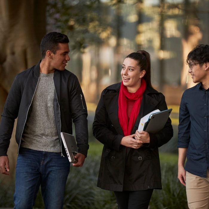 Three law students walking in front of Law Building, walking towards the camera, greenary and reflections in glass of Law Building in background