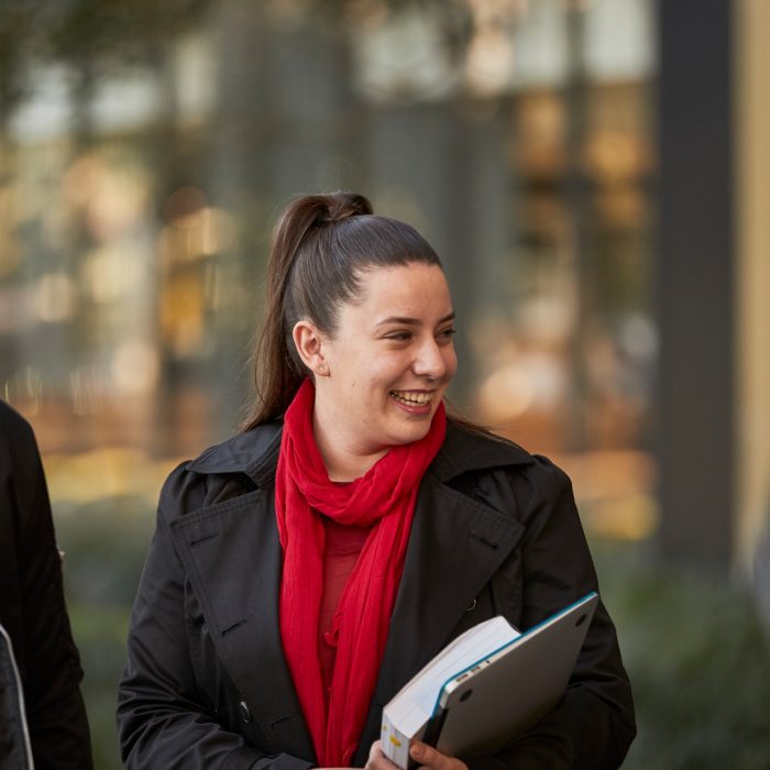 Three law students walking in front of Law Building, walking towards the camera, greenary and reflections in glass of Law Building in background