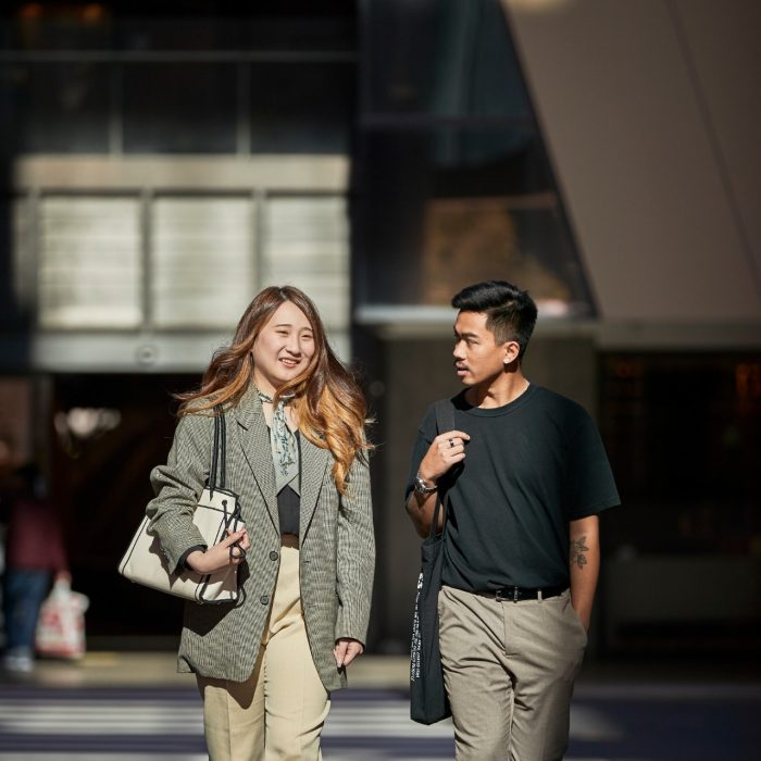 Female in green jacket and male in black t-shirt, law students, walking together behind the law building.  Shadows and light on buildinf exterior.