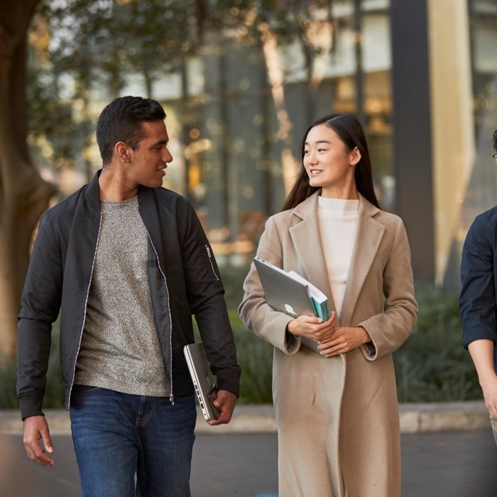 Three law students walking in front of Law Building, walking towards the camera, greenary and reflections in glass of Law Building in background