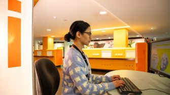 A librarian at the Help Zone next to a large column. A large 'i' is printed on the column, representing 'information'.