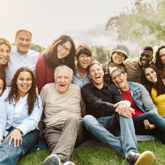 Happy multigenerational people having fun sitting on grass in a public park