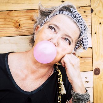 Alternative unusual pretty senior caucasian lady with trendy make up and grey hair blowing a pink bubble gum and looking up - nice portrait of old youth people enjoying the life