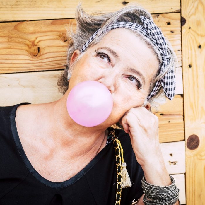 Alternative unusual pretty senior caucasian lady with trendy make up and grey hair blowing a pink bubble gum and looking up - nice portrait of old youth people enjoying the life