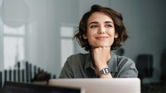 Image of young beautiful joyful woman smiling while working with laptop in office