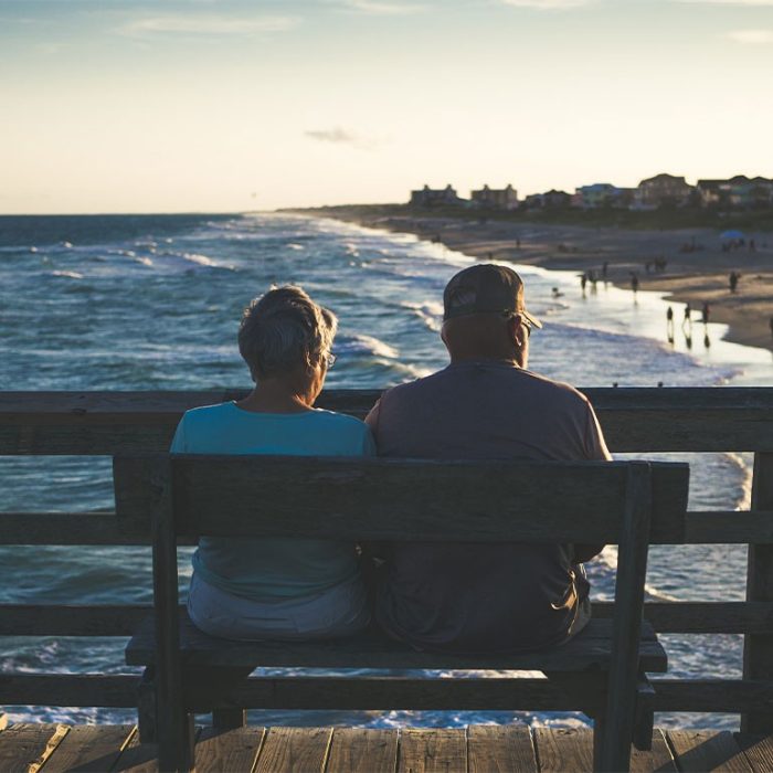 Elderly couple sitting on bench next to ocean