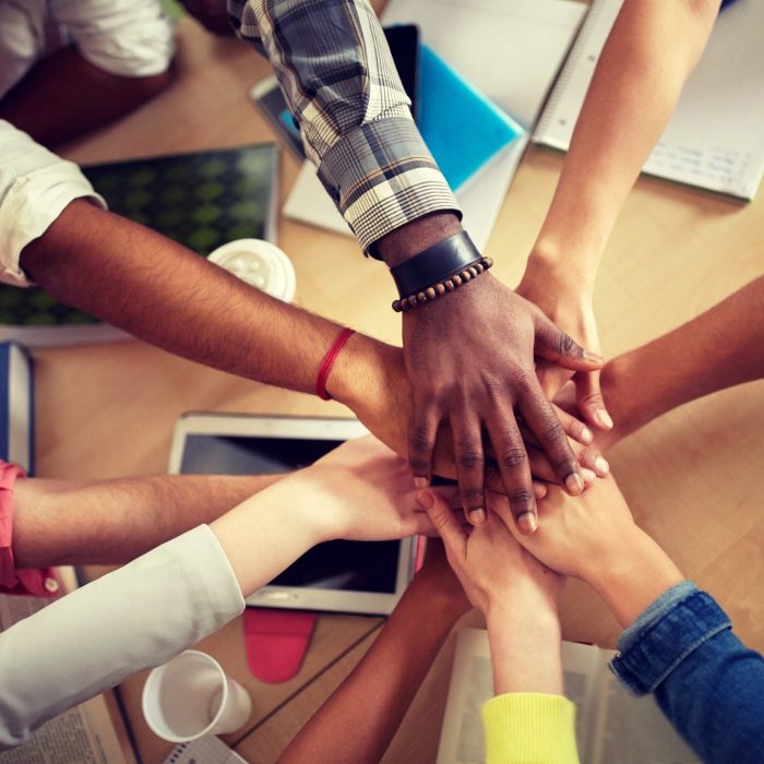 education, school, teamwork and people concept - close up of international students with hands on top of each other sitting at table