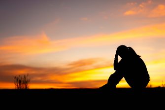 Young woman using electric fan at home in living room, sitting on couch cooling off during hot weather, suffering from heat, high temperature