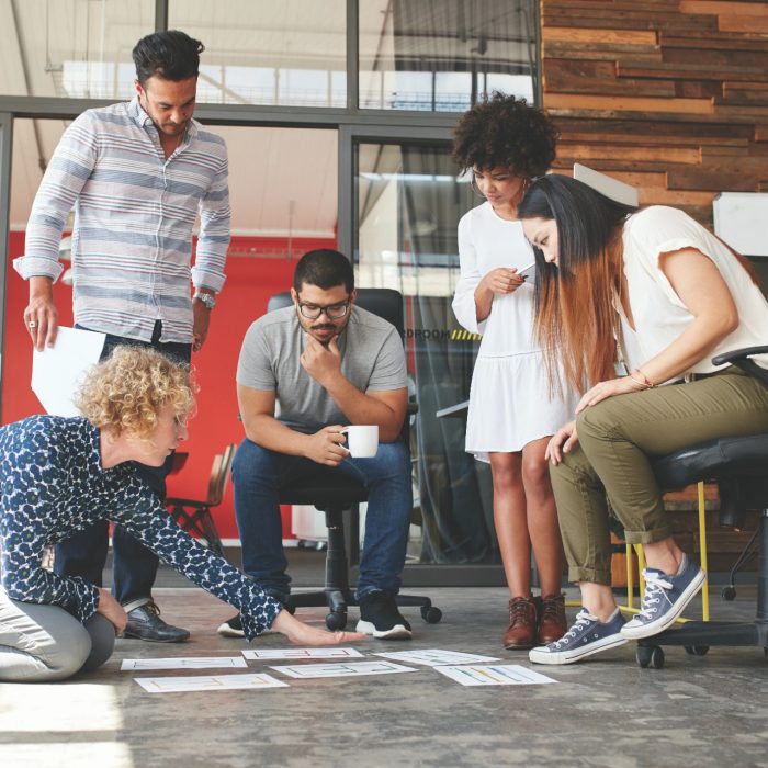 Creative people looking at project plan laid out on floor. Mixed race business associates discussing new project plan in modern office.