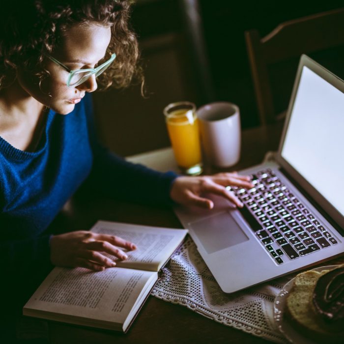 Young female student studying from a book and using laptop