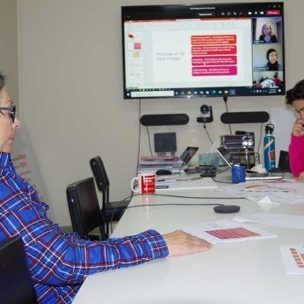 Two people are sitting at a conference table in a virtual meeting
